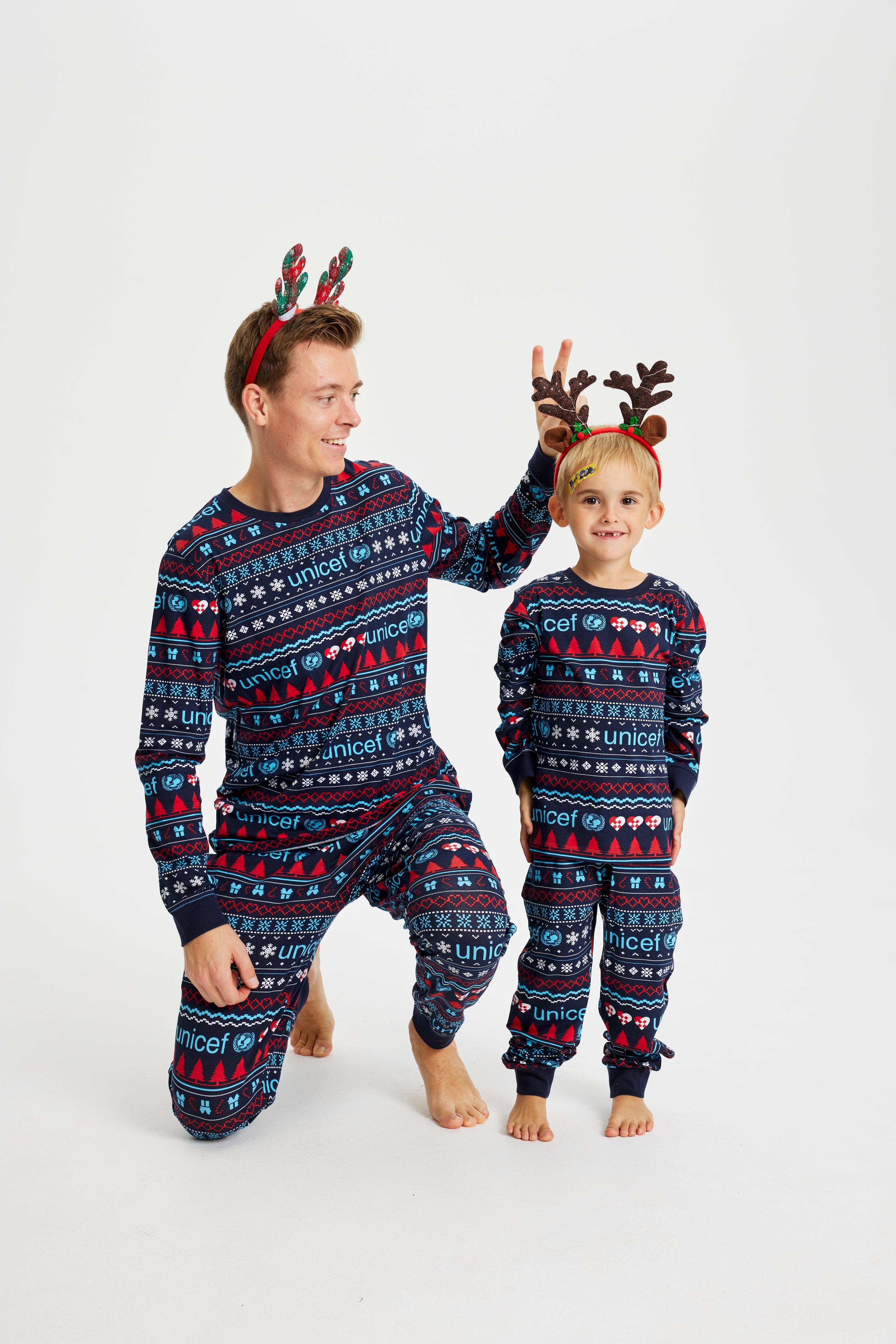 En mand sidder på knæ ved siden af et barn, mens begge er iført samme julepyjamas.